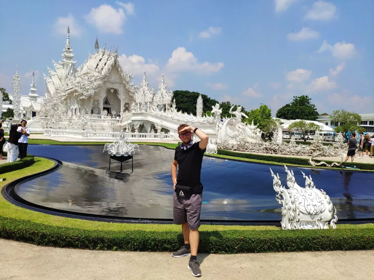 Mężczyzna pozuje przed olśniewającą Białą Świątynią w Chiang Rai. Woda odbija jej biel, tworząc magiczny widok.