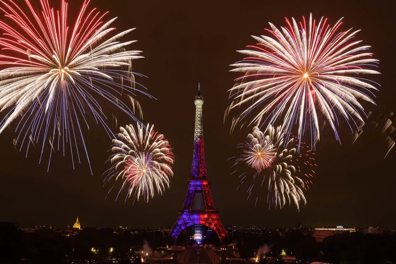 Feu d'artifice spectaculaire illuminant la Tour Eiffel, parée des couleurs de la France, dans le ciel nocturne de Paris.