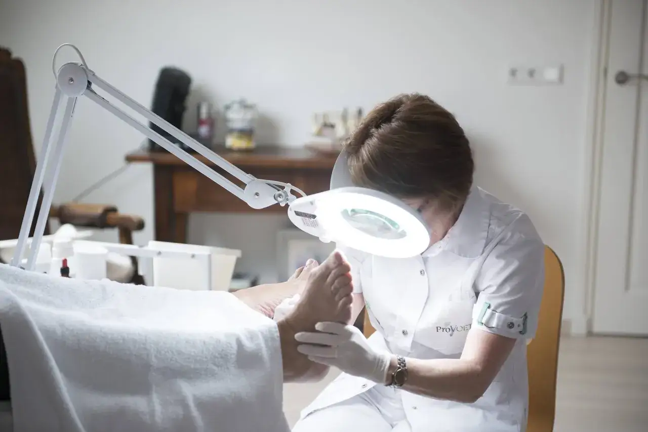 Podologue examine un pied sous une lampe loupe. Le tarif pour une mycose est abordable.