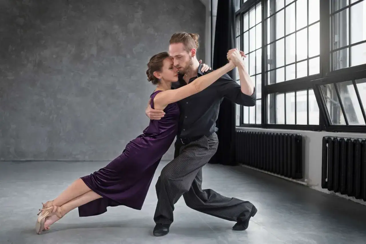 Para tańczy tango, wykonując eleganckie tańce standardowe. Kobieta w fioletowej sukni i mężczyzna w czarnej koszuli i szarych spodniach.