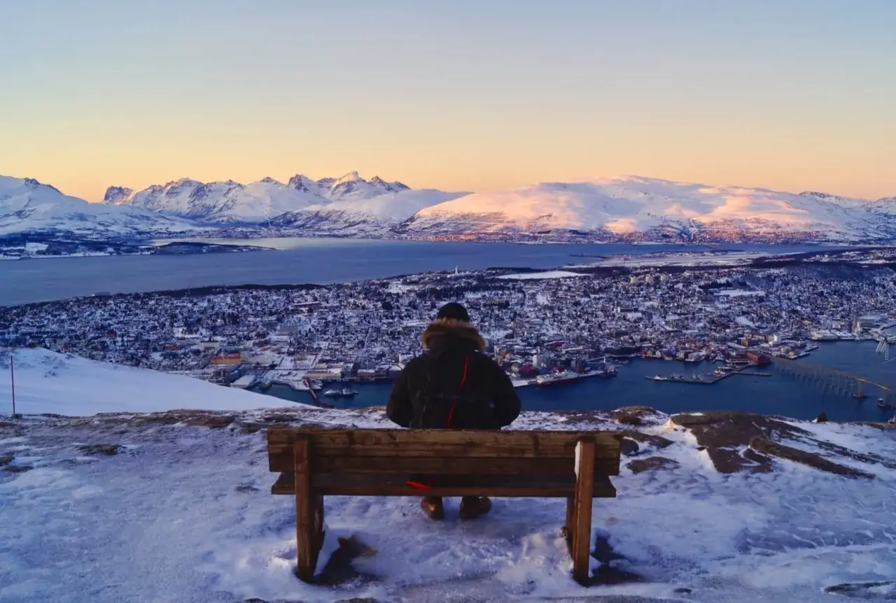 Ein Mann sitzt auf einer Bank und blickt auf das verschneite Troms&oslash;. Ein perfekter Ort f&uuml;r Troms&oslash; Geheimtipps.