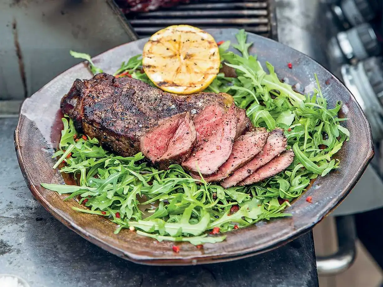 Perfekt grillad ryggbiff, skivad och serverad på en bädd av ruccola med en grillad citronklyfta.