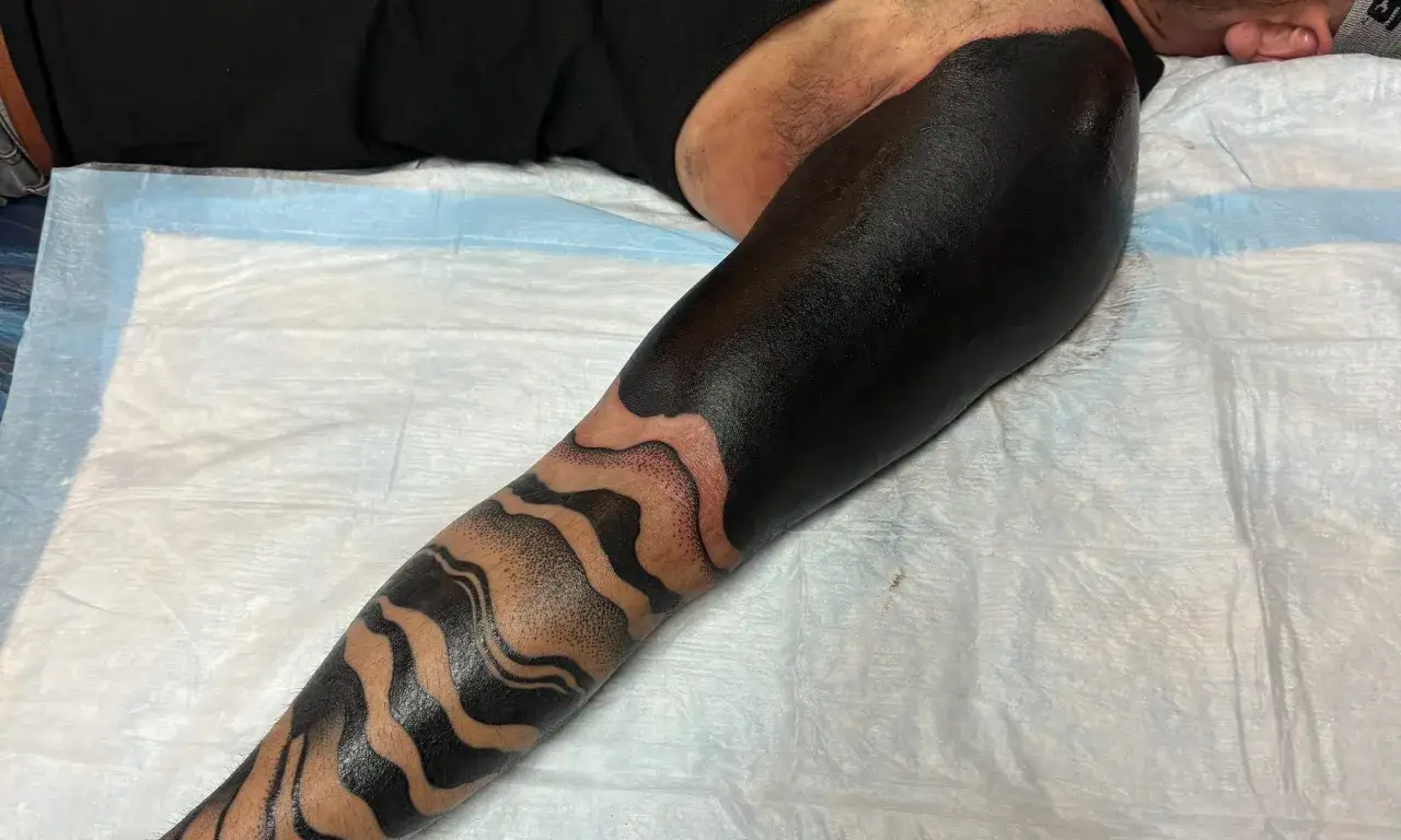 Ein Unterarm mit einem auff&auml;lligen all black tattoo, das in Wellenmuster &uuml;bergeht.