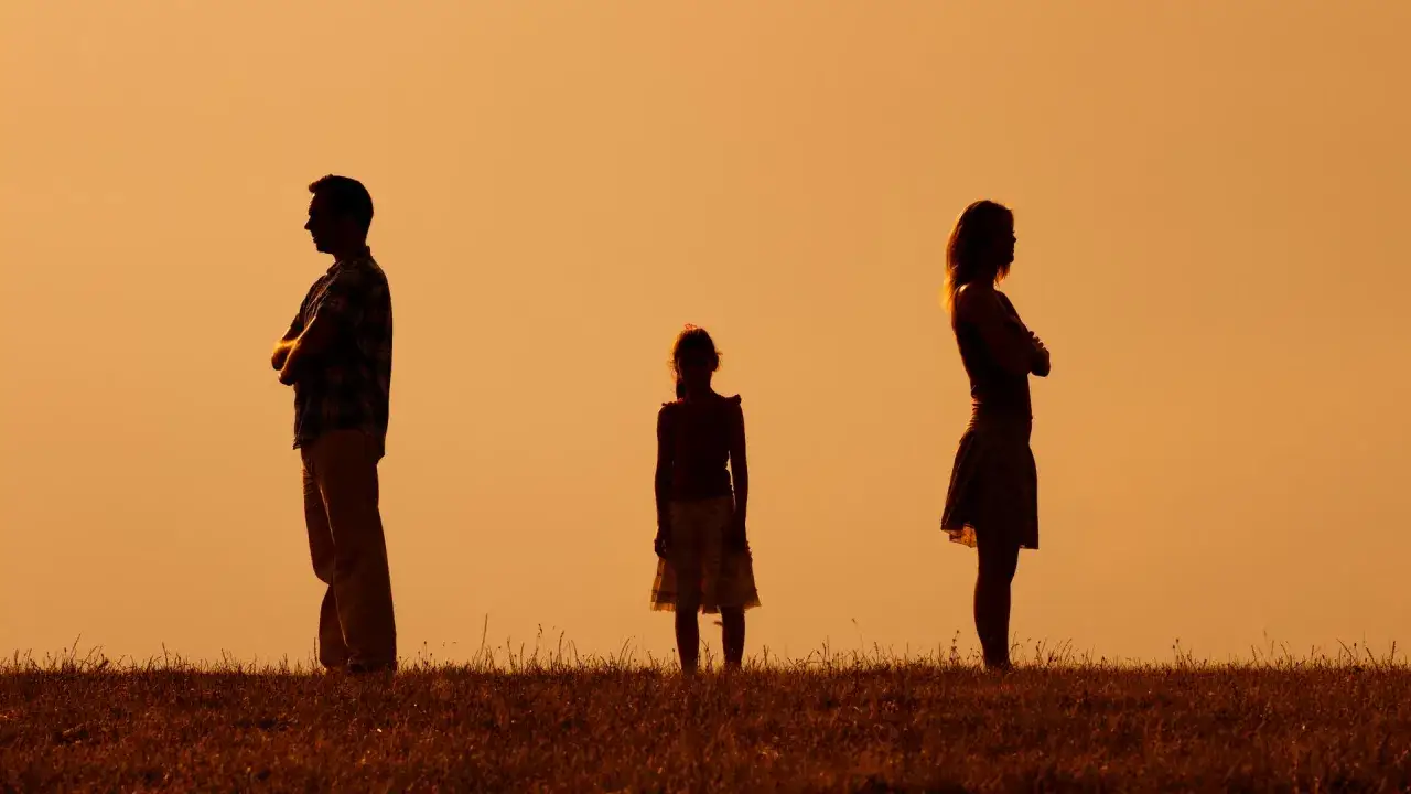 Silhouetten von Eltern, die sich abwenden, während ihr Kind dazwischen steht. Ein Bild, das ein Trennungsjahr mit Kindern symbolisiert.