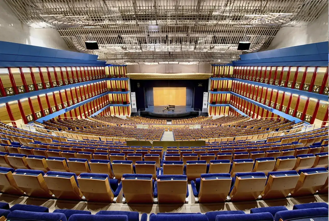 Gran auditorio con asientos azules y escenario listo para la programaci&oacute;n del palacio de festivales.