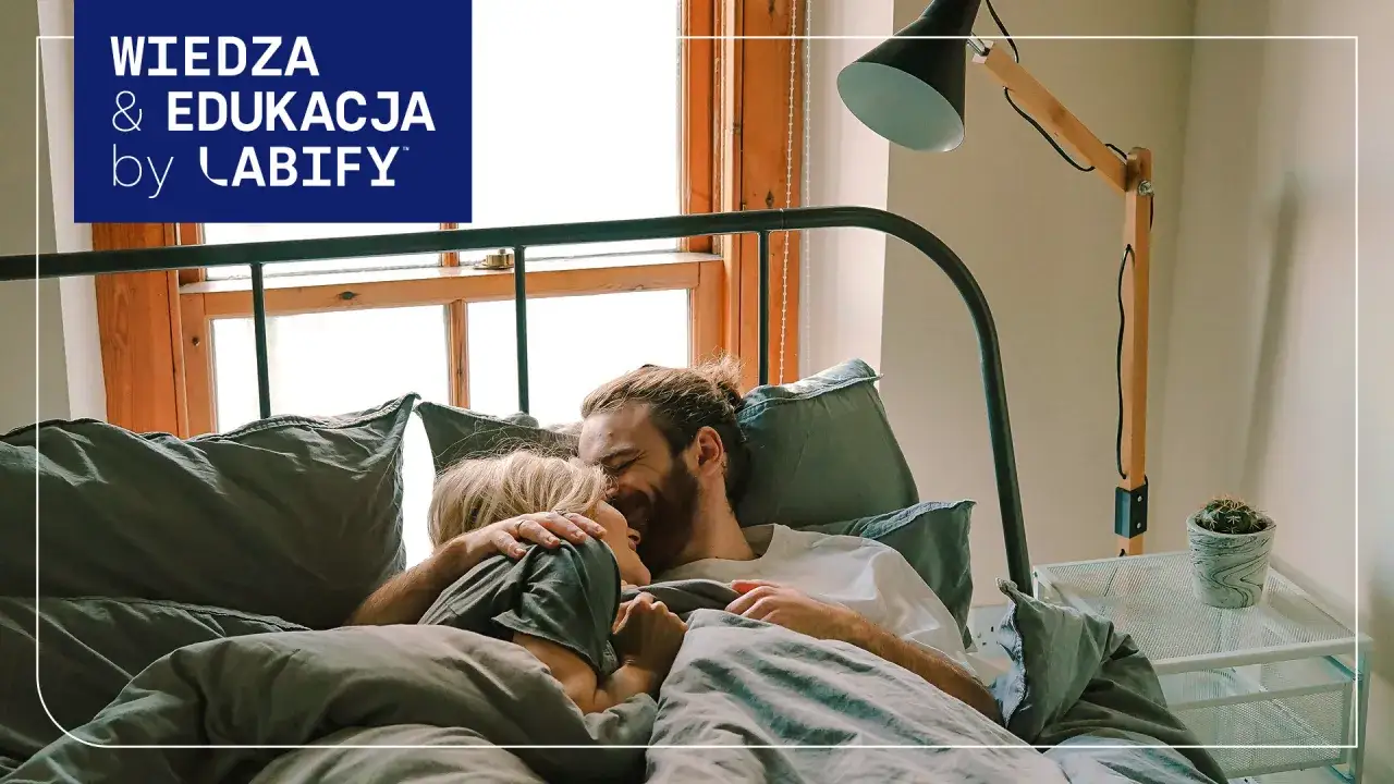 Para, przytulająca się w łóżku, uśmiechnięta. Czy to przejaw libido? Wiedza & Edukacja by LABIFY.