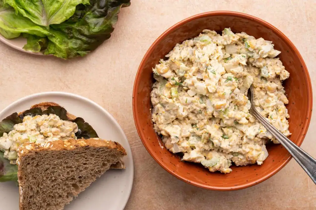 Ensalada cremosa de garbanzos, alternativa vegana al atún, servida en un bol y en un sándwich con pan integral y lechuga.