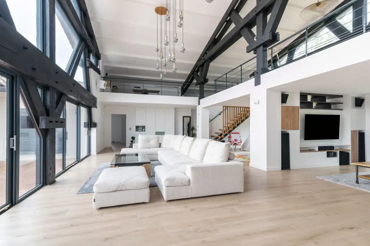 Salon moderne avec poutres apparentes, canapé blanc, escalier en bois. Le prix de rénovation de maison peut varier selon l'ampleur des travaux.