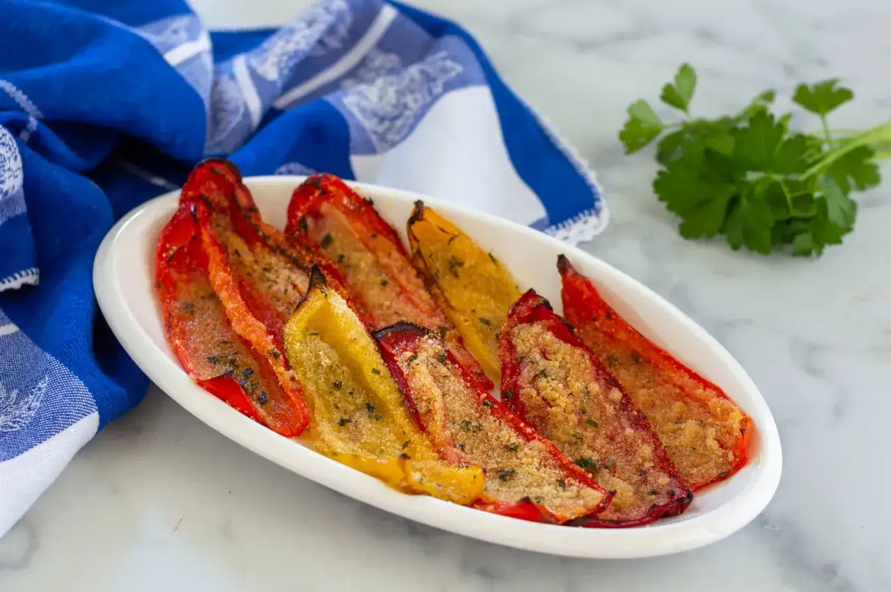Peperoni gratinati al forno, rossi e gialli, cotti alla perfezione con pangrattato e erbe aromatiche, serviti su un piatto bianco.