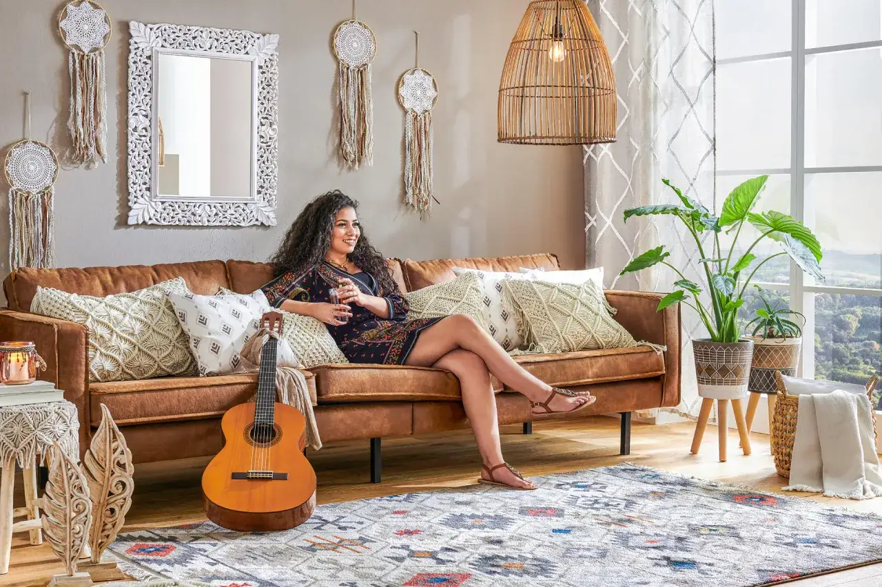 En kvinna vilar i en mysig soffa, omgiven av olika inredningsstilar som boho och bohemiskt. En gitarr och dr&ouml;mf&aring;ngare bidrar till den avslappnade atmosf&auml;ren.