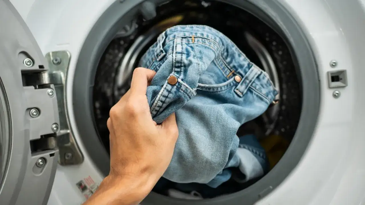 Mano che inserisce jeans chiari nella lavatrice, sperando che non si restringano troppo.