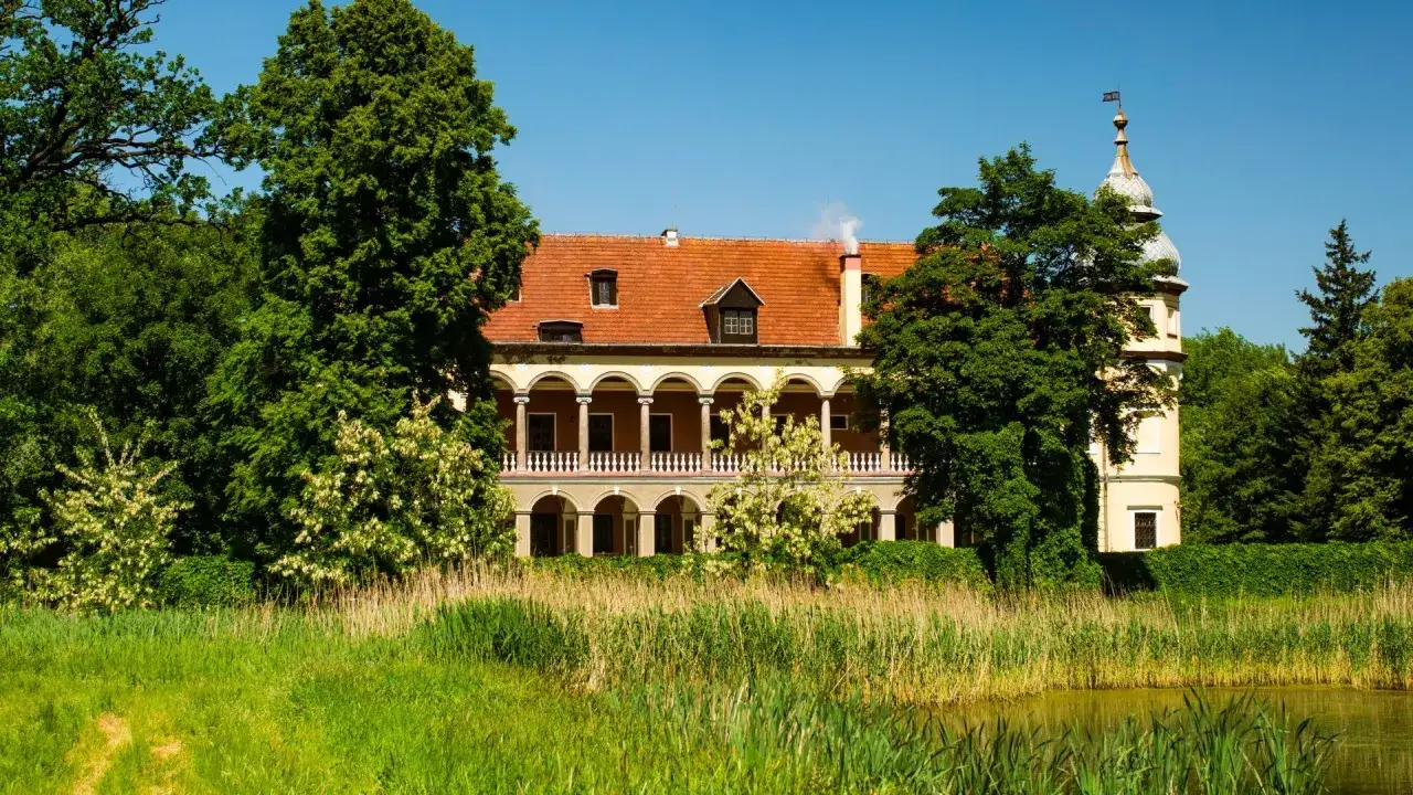 Pałac w Krobielowicach otoczony zielenią, z charakterystyczną arkadową loggią i wieżyczką.