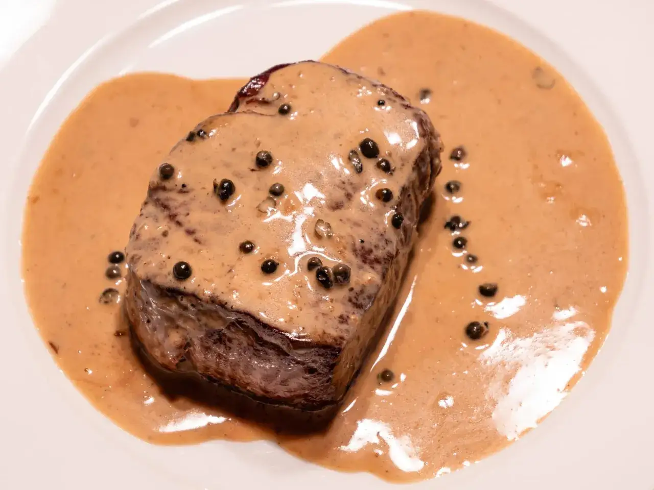 Un steak de bœuf généreusement nappé d'une onctueuse sauce au poivre, parsemée de grains de poivre noir.