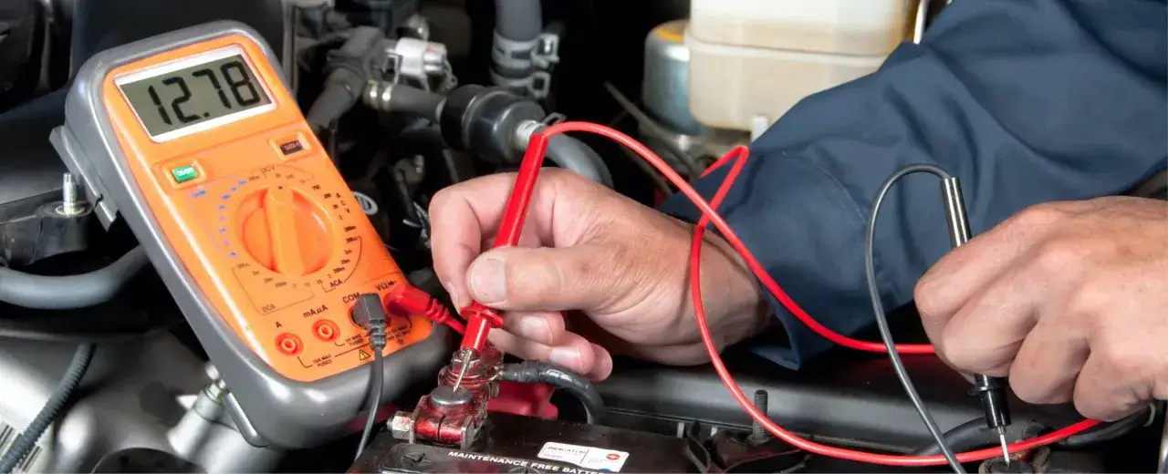 Mechanik sprawdza napięcie akumulatora multimetrem. Wynik 12.78V wskazuje na jego stan.
