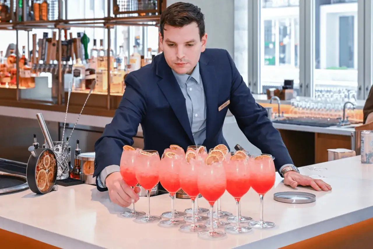 El director de alimentos y bebidas supervisa cócteles rosados con rodajas de naranja en una barra.