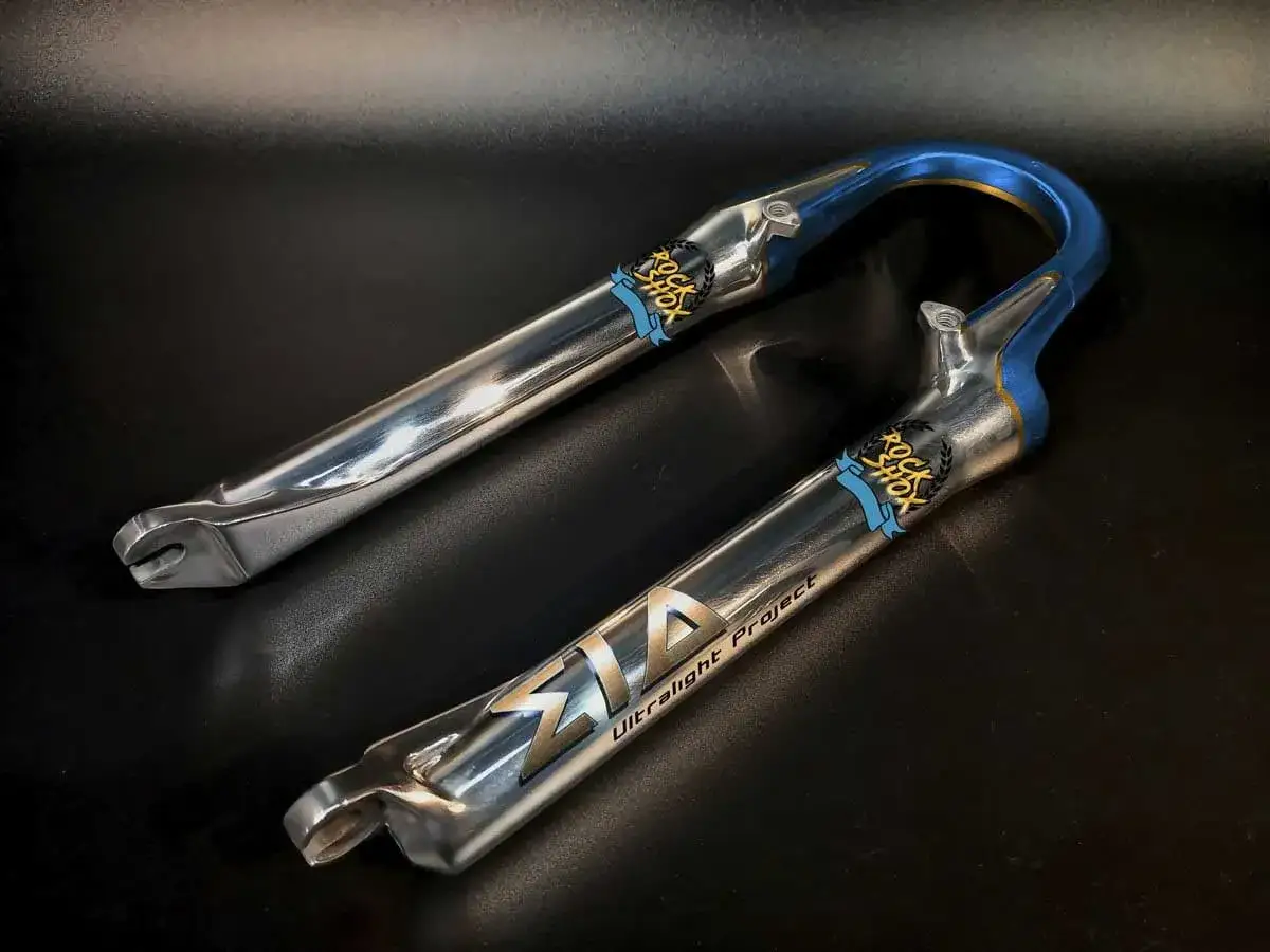 Błyszczące, chromowane golenie widelca rowerowego Rock Shox z niebieskimi akcentami, idealne do tuningu roweru.