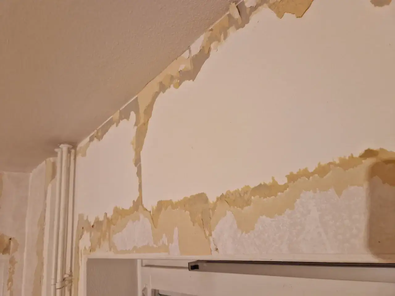 Underarbete för tapetsering: gammal tapet flagnar och lämnar ojämna ytor på väggen.