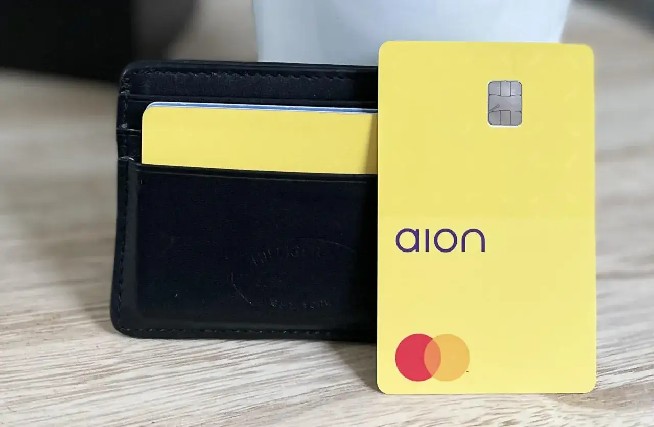 Żółta karta płatnicza Aion Bank z logo Mastercard obok czarnego portfela.