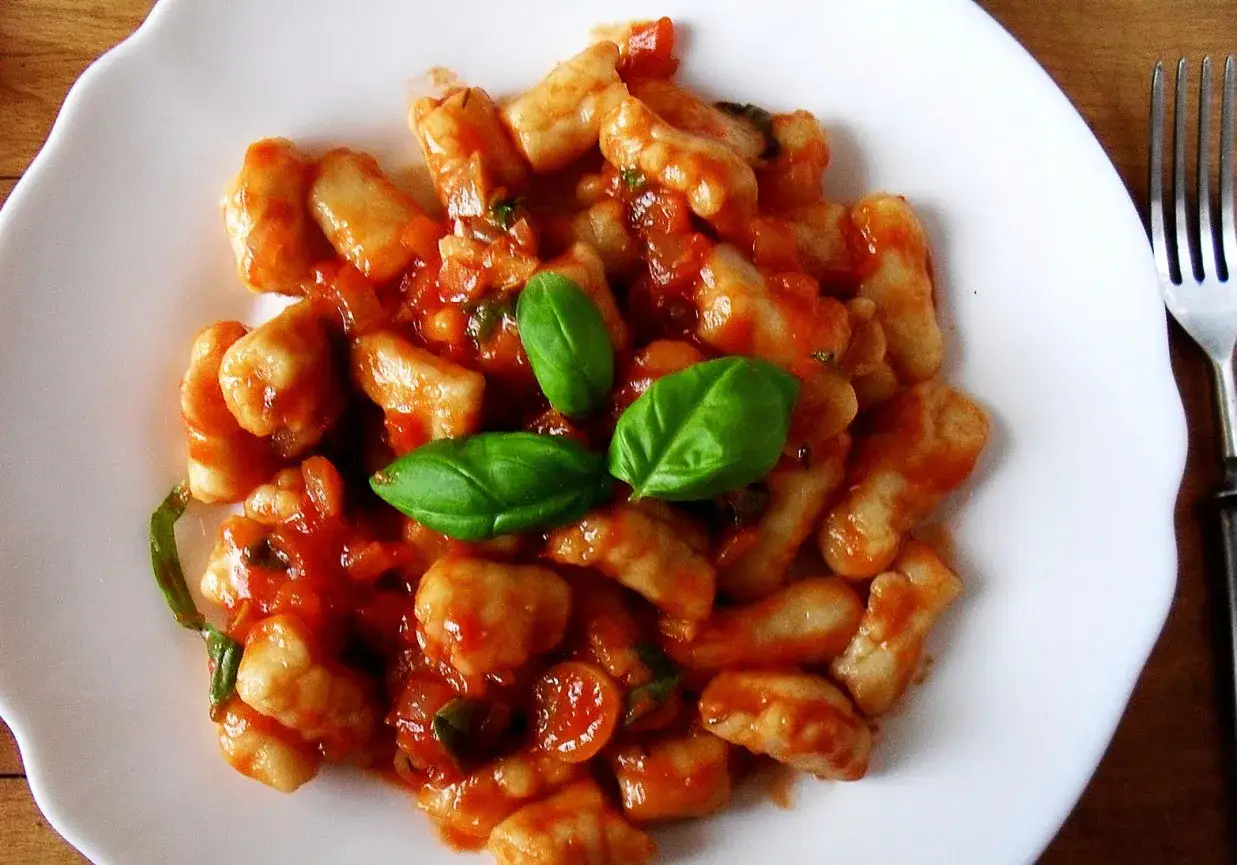 Pyszne gnocchi w sosie pomidorowym z bazylią, podane na białym talerzu.