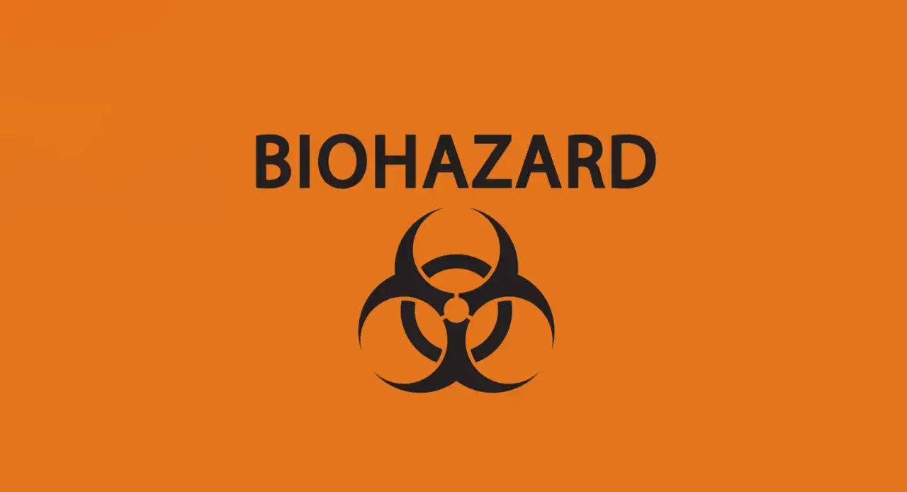 Pomarańczowe tło z czarnym symbolem biohazard i napisem BIOHAZARD. Ostrzeżenie przed zagrożeniem biologicznym.