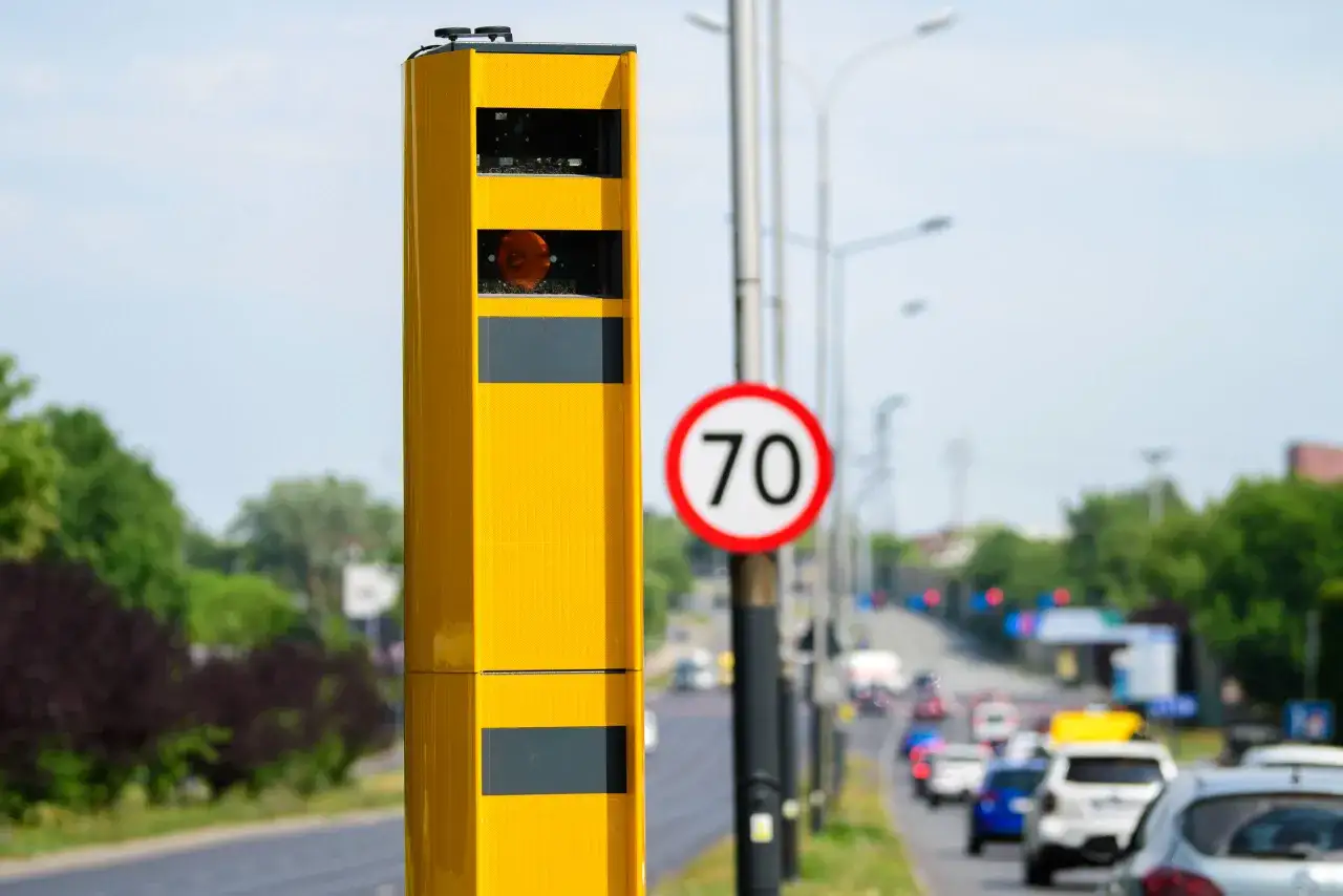Żółty fotoradar przy drodze z ograniczeniem do 70 km/h. Urządzenie monitoruje prędkość pojazdów, pokazując, jak działa fotoradar.
