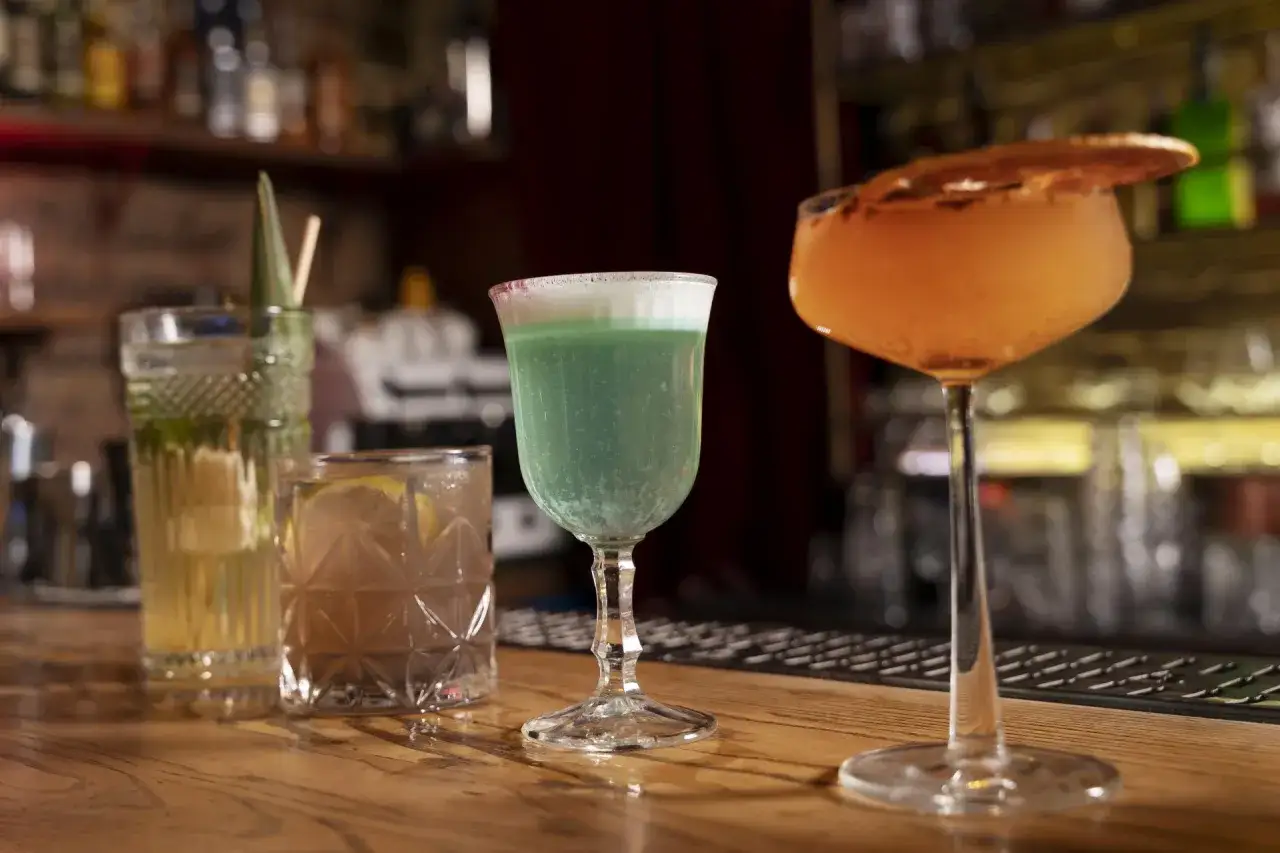 Zielony drink z pianką i pomarańczowy koktajl z plasterkiem cytrusa na barze. Może to być drink z brandy.