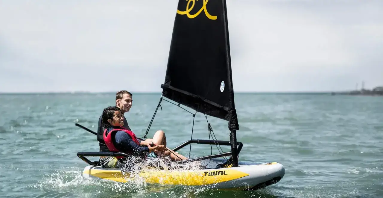 Couple souriant naviguant sur un voilier transportable gonflable, éclaboussures d'eau, mer calme.