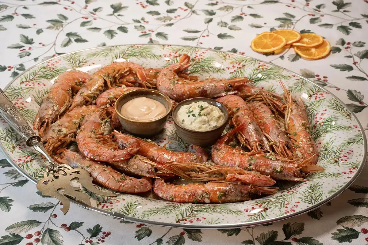 Gambones al horno servidos en una bandeja festiva con dos salsas y rodajas de naranja deshidratada.