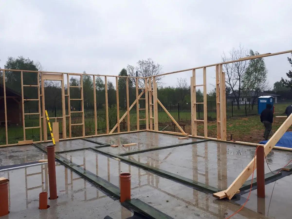 Budowa domu szkieletowego: fundament pod słupy drewniane, ściany w trakcie montażu, widoczne instalacje.