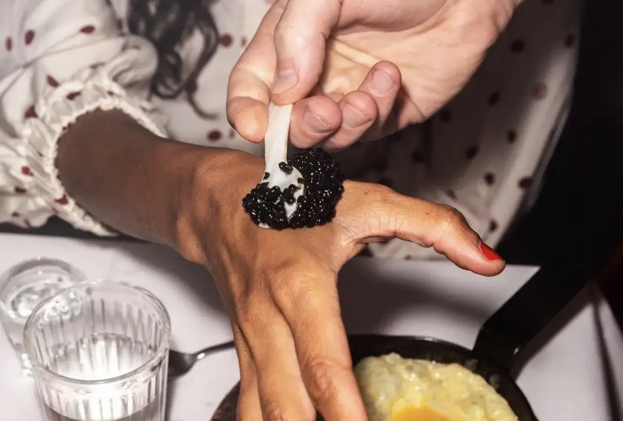 En hand l&auml;gger kaviar p&aring; en annan hand som en del av en unik matupplevelse p&aring; restaurang Punk Royale.