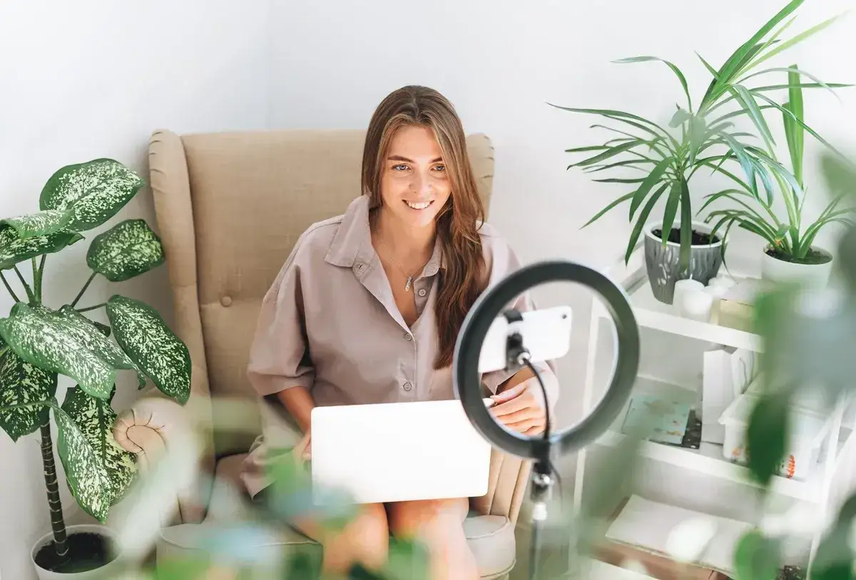 Uśmiechnięta kobieta z laptopem i ring light, przygotowuje się do nagrania, planując wsp&oacute;łpracę barterową.