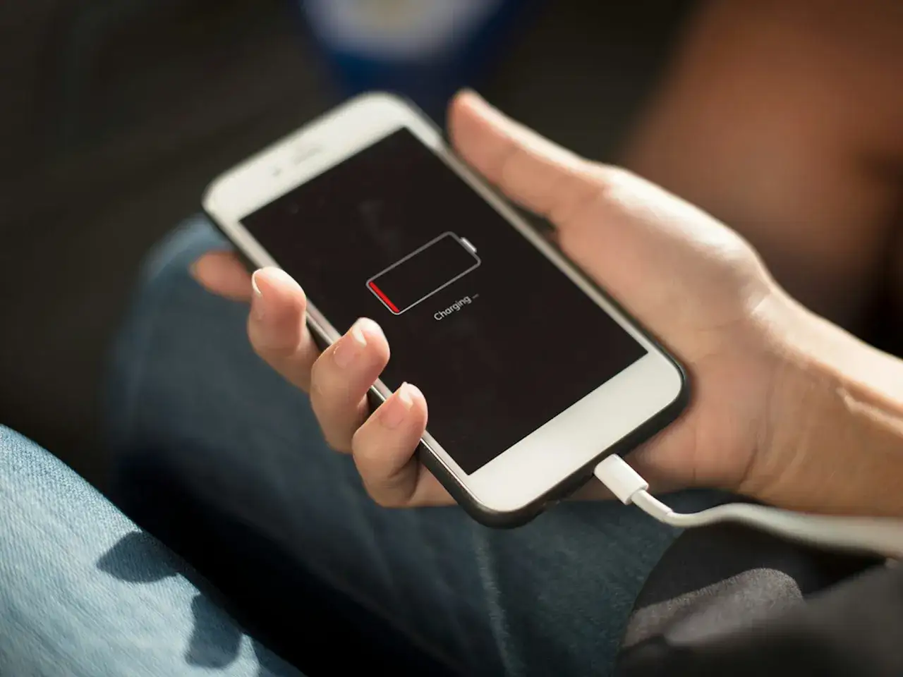 En hand h&aring;ller en mobil som laddas. Batteriikonen visar att mobilen drar batteri p&aring; natten, trots laddkabeln.