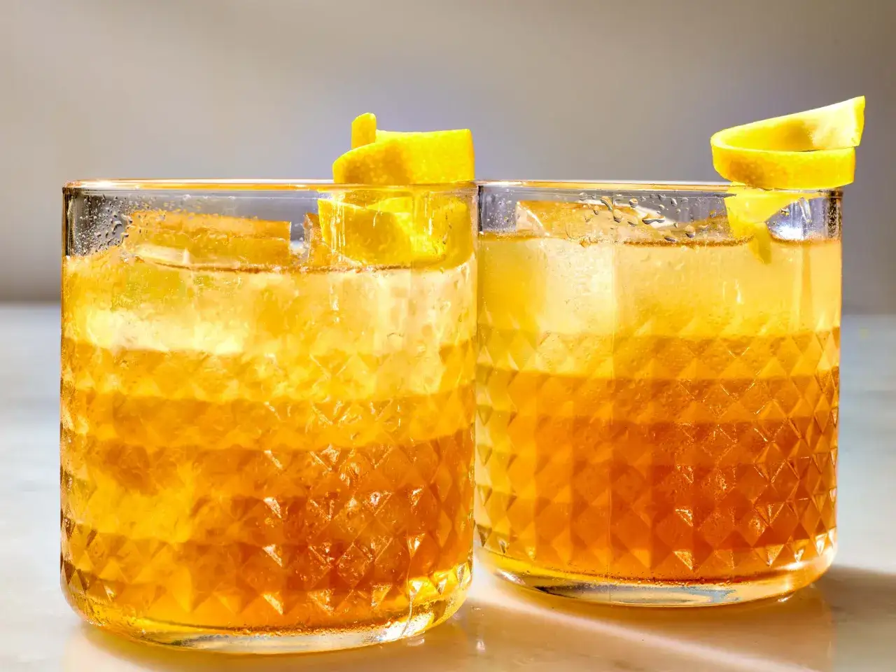 Två glas med en gyllene drink, is och citronskal. En perfekt