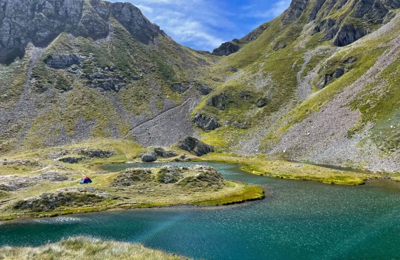 Tenda rossa e blu tra i laghetti di Ponteranica, circondati da montagne verdi e rocciose sotto un cielo azzurro.