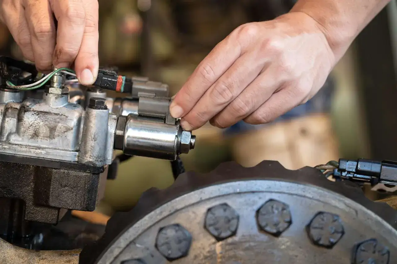 Mechanic's hands connect a wire harness to a solenoid, possibly addressing bad solenoid symptoms.