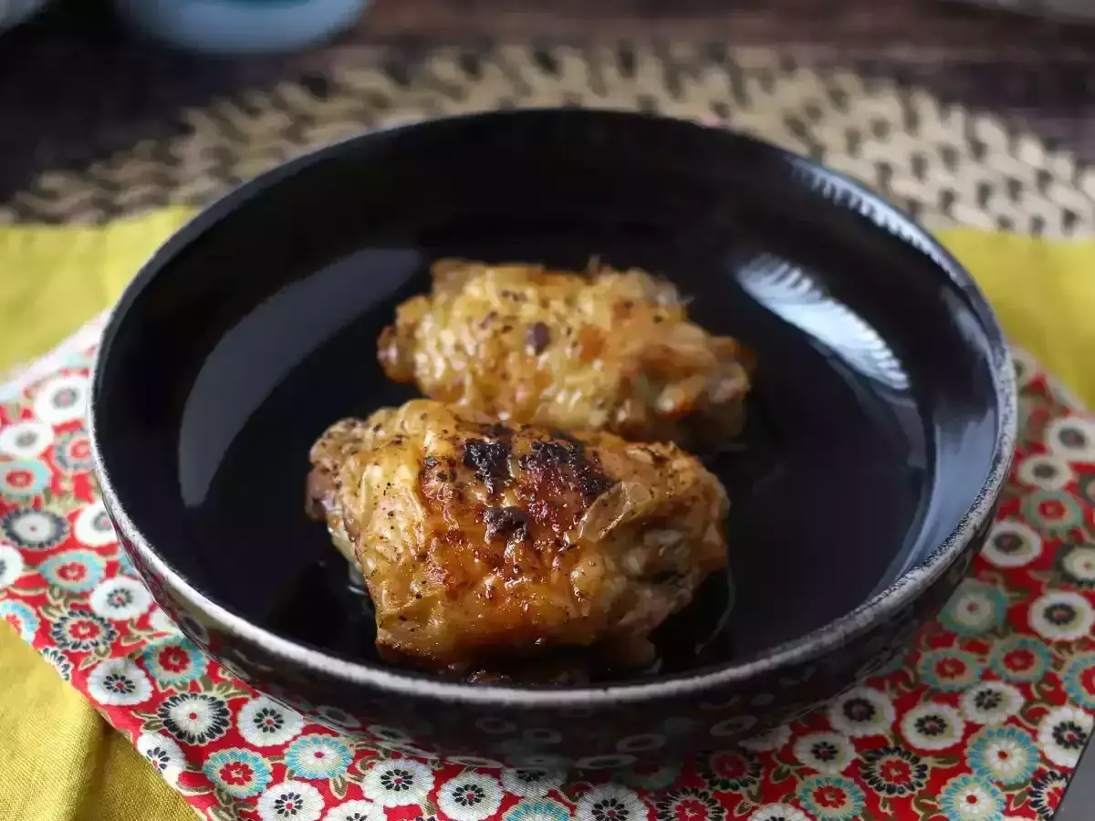 Dwa soczyste skrzydełka kurczaka, idealnie przyrządzone w airfryer, podane w czarnej misce na kolorowej serwetce.