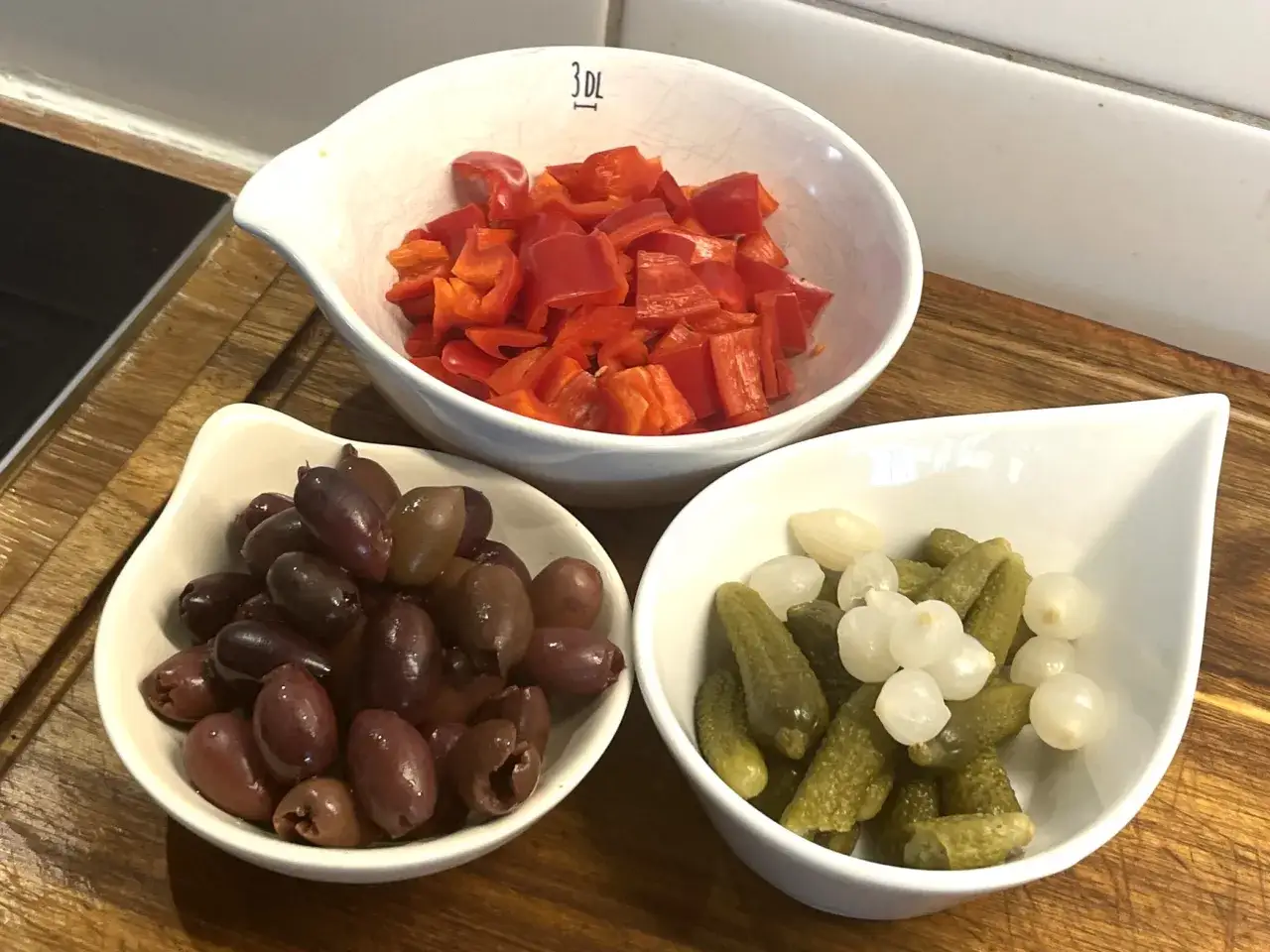 F&ouml;rberedelser f&ouml;r en smakrik kreolsk gryta: skivad r&ouml;d paprika, oliver och cornichoner med sm&aring; l&ouml;kar.