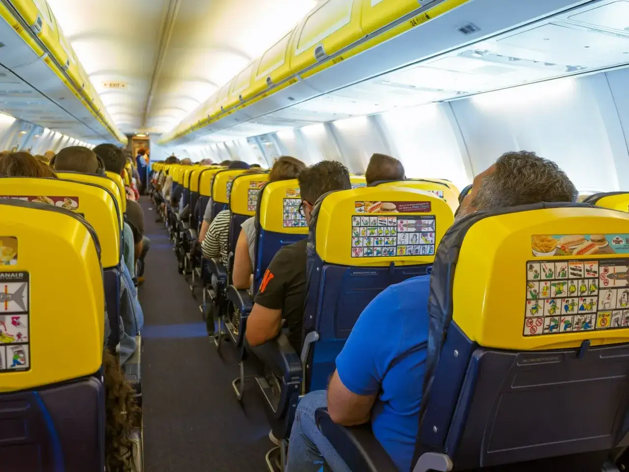 Wnętrze samolotu Ryanair, pasażerowie siedzą w rzędach. Widok z perspektywy siedzącego pasażera, jak wygląda odprawa Ryanair.