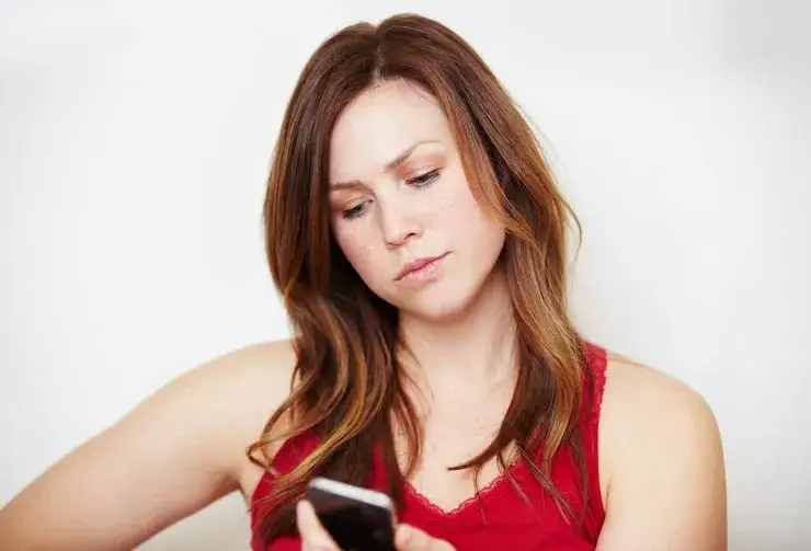 Zmartwiona kobieta patrząca na telefon, symbolizująca dyskomfort