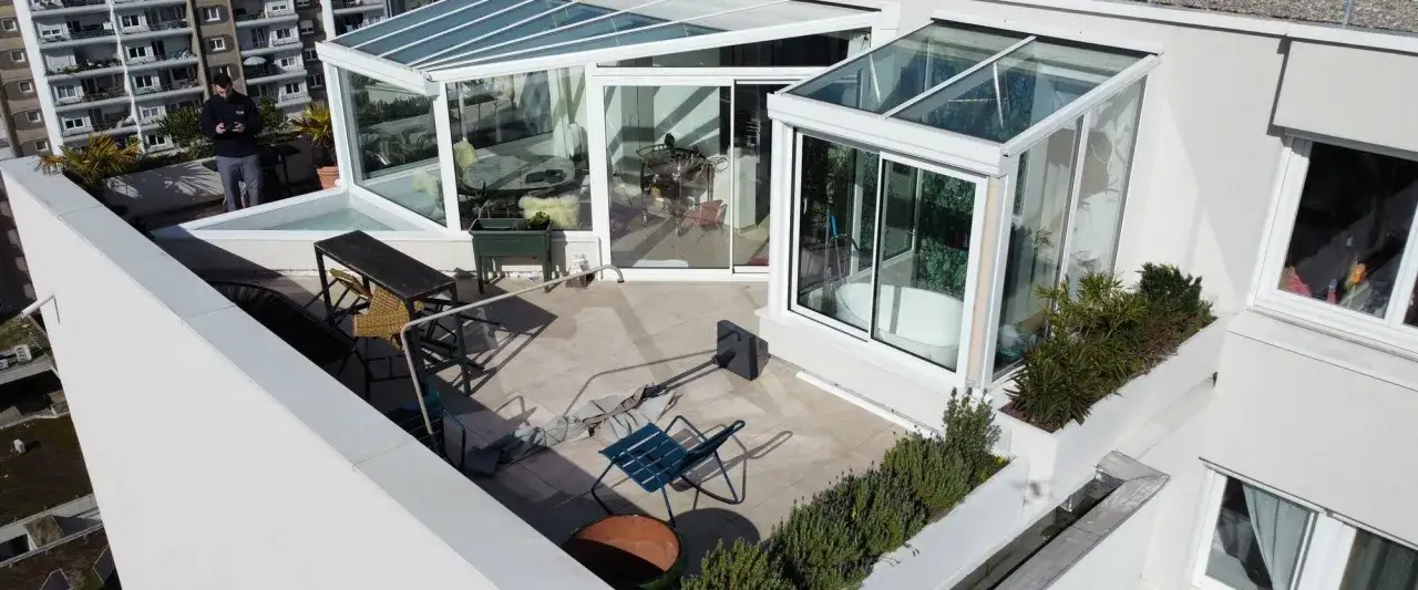 Terrasse d'un appartement avec une véranda moderne, un jacuzzi, des meubles de jardin et un homme regardant son téléphone.