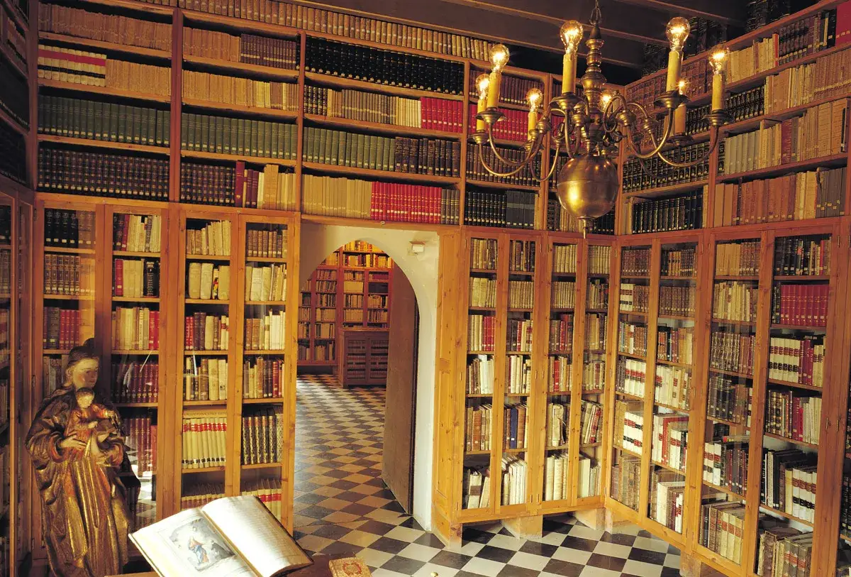 Interior del museu del castell de Peralada, con estanterías repletas de libros antiguos y una lámpara de araña dorada.