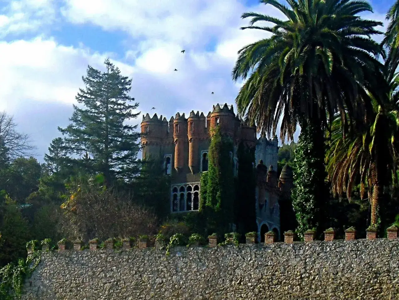 El palacio de Ocharan, un castillo de cuento rodeado de vegetación exuberante y palmeras, se alza majestuoso bajo un cielo azul con nubes.