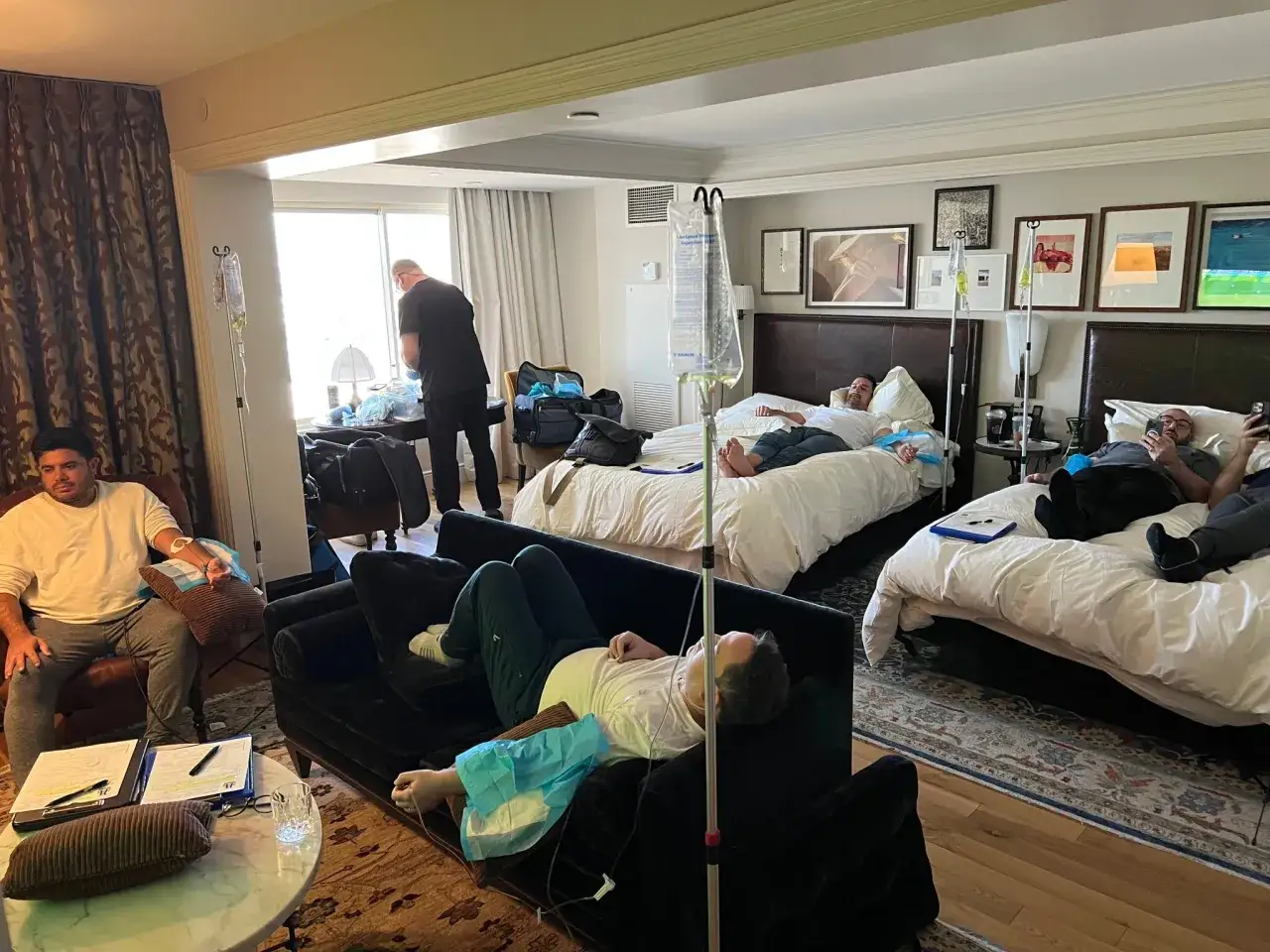 Men are sleeping off a hangover in a hotel room, receiving IV drips.