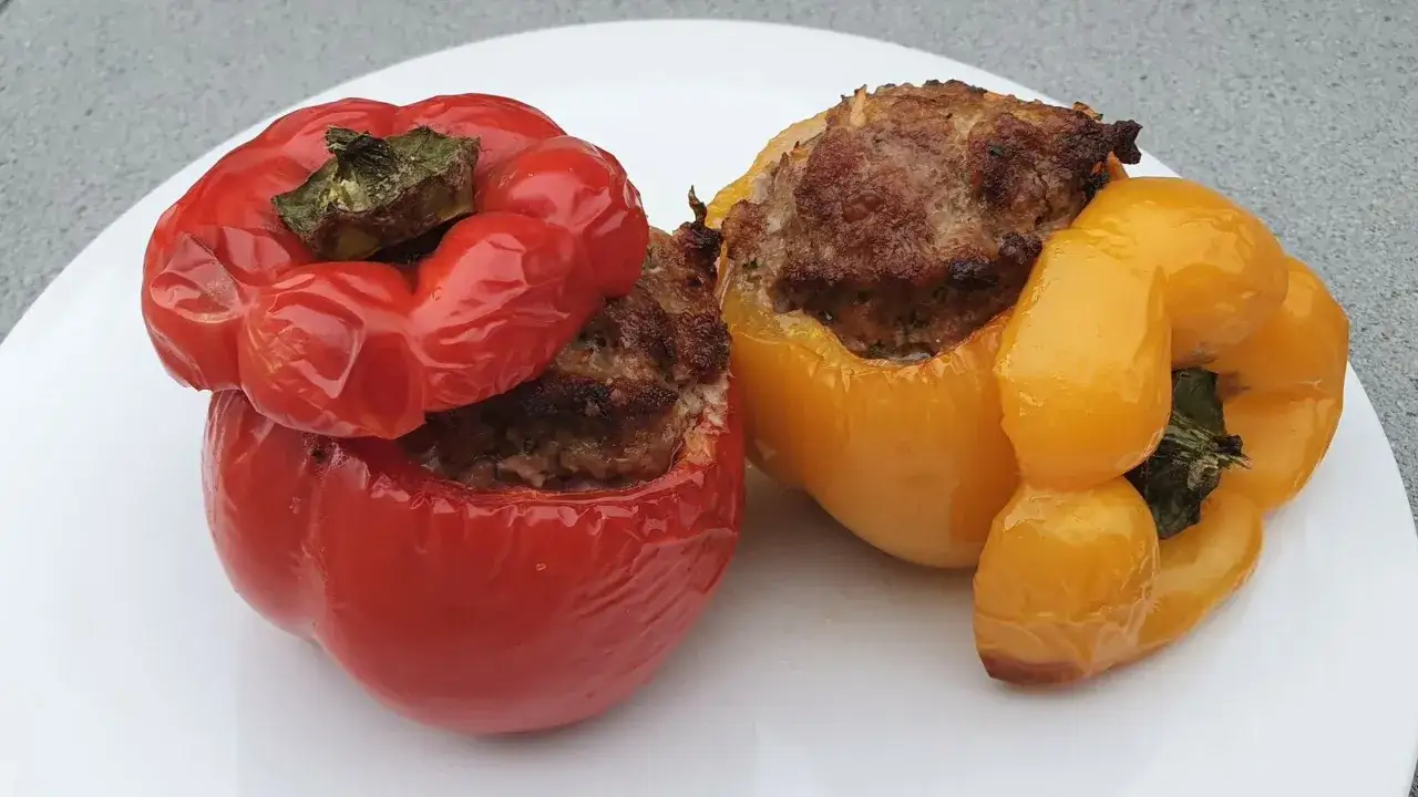 Deux poivrons farcis, un rouge et un jaune, sont présentés sur une assiette blanche. La garniture de viande est visible et dorée.