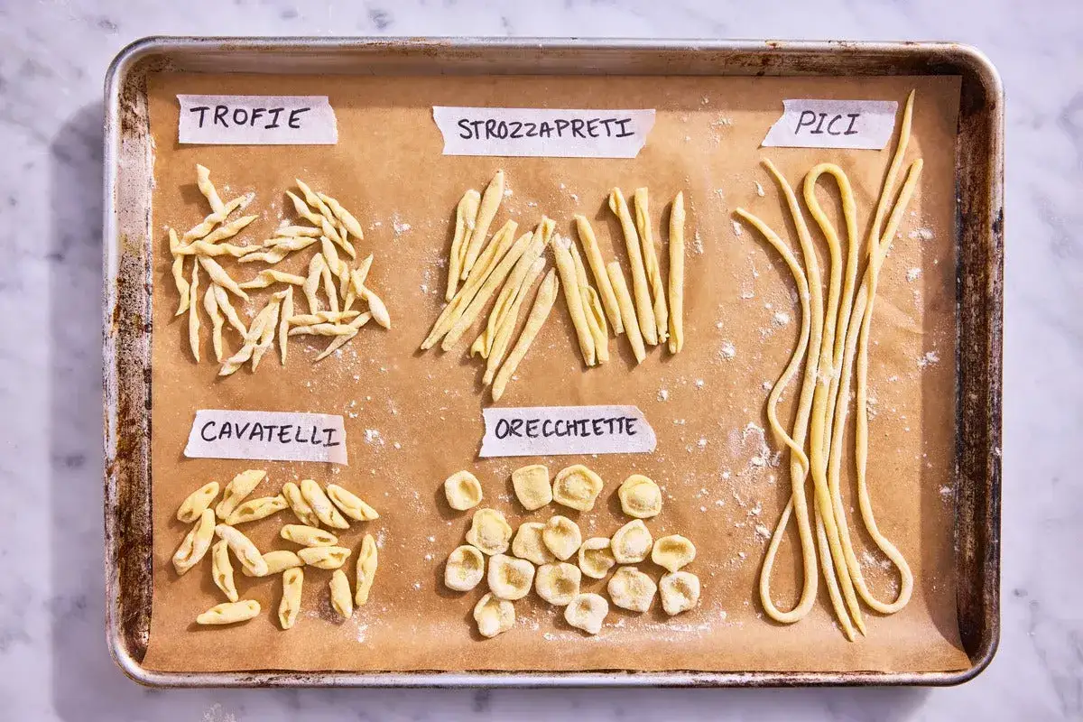 F&uuml;nf verschiedene **Nudelformen** auf Backpapier: Trofie, Strozzapreti, Pici, Cavatelli und Orecchiette.