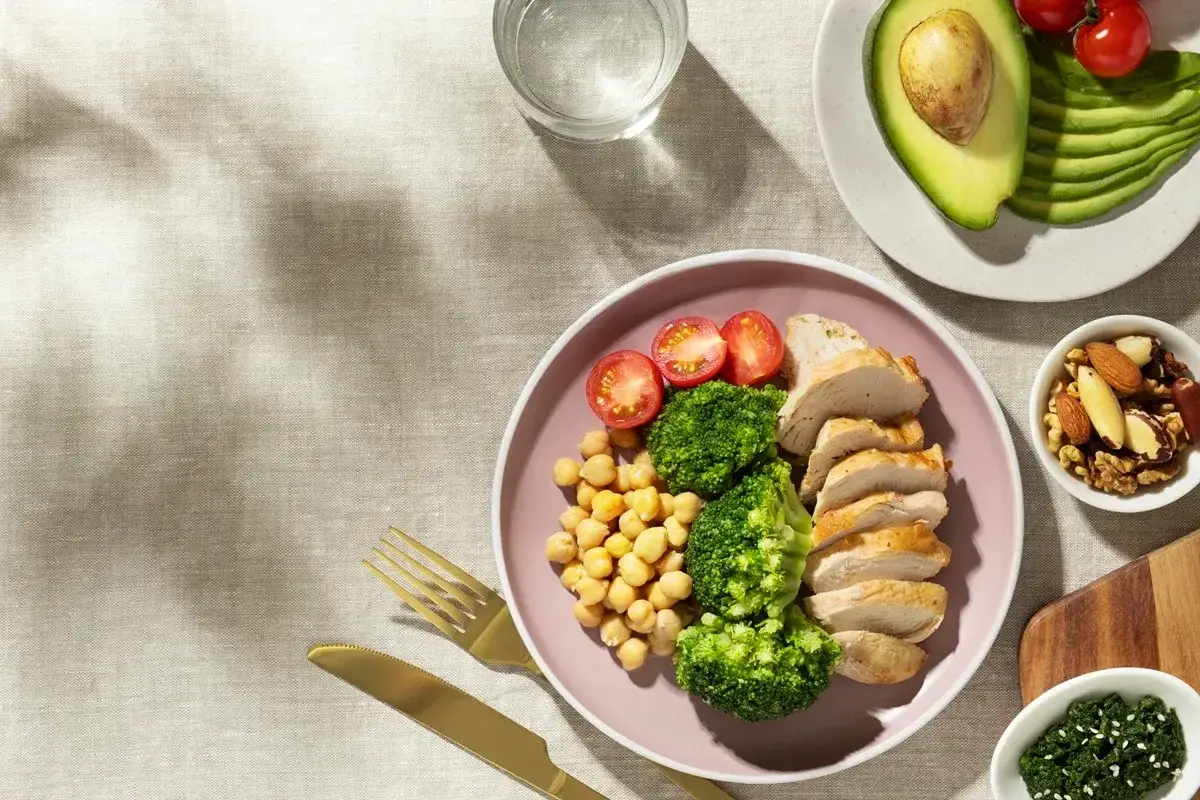 Assiette de poulet, brocolis, pois chiches et tomates, idéale pour une prise de masse musculaire rapide. Avocat et noix à côté.