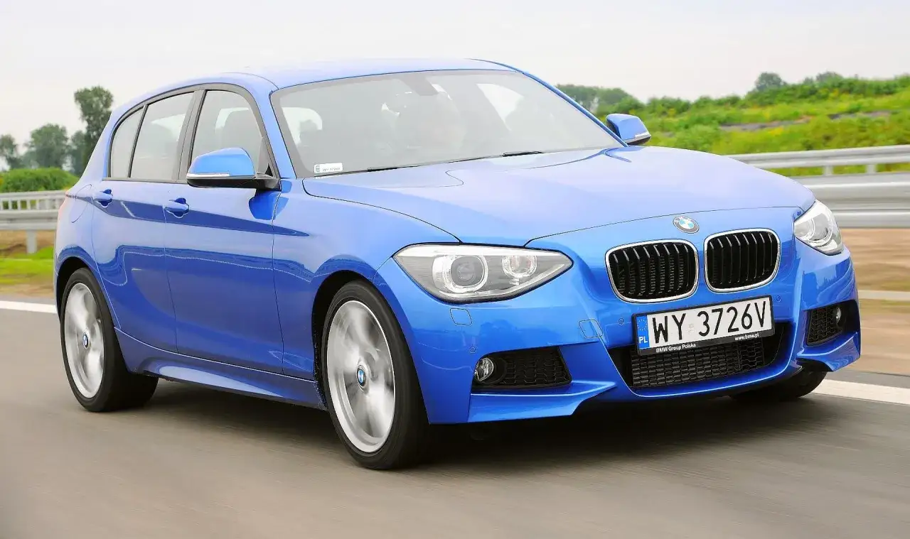 Niebieskie BMW 116i pędzi po drodze, kierowca w kasku za kierownicą.