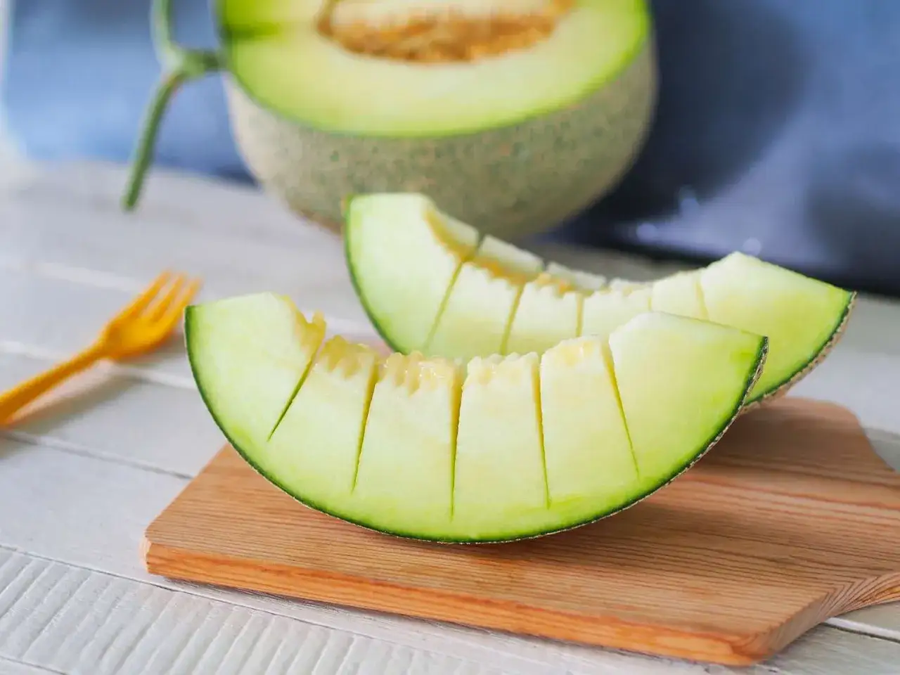 Tv&aring; saftiga skivor honungsmelon, nyttigt och uppfriskande, ligger p&aring; en tr&auml;sk&auml;rbr&auml;da. En hel melon syns i bakgrunden.