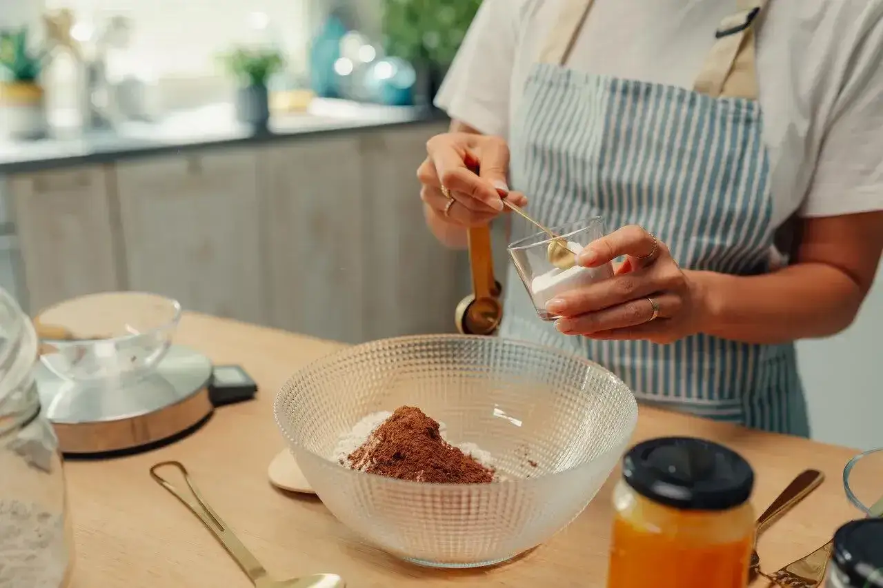 Kobieta dodaje sodę oczyszczoną do miski z mąką i kakao. Szuka co zamiast proszku do pieczenia?