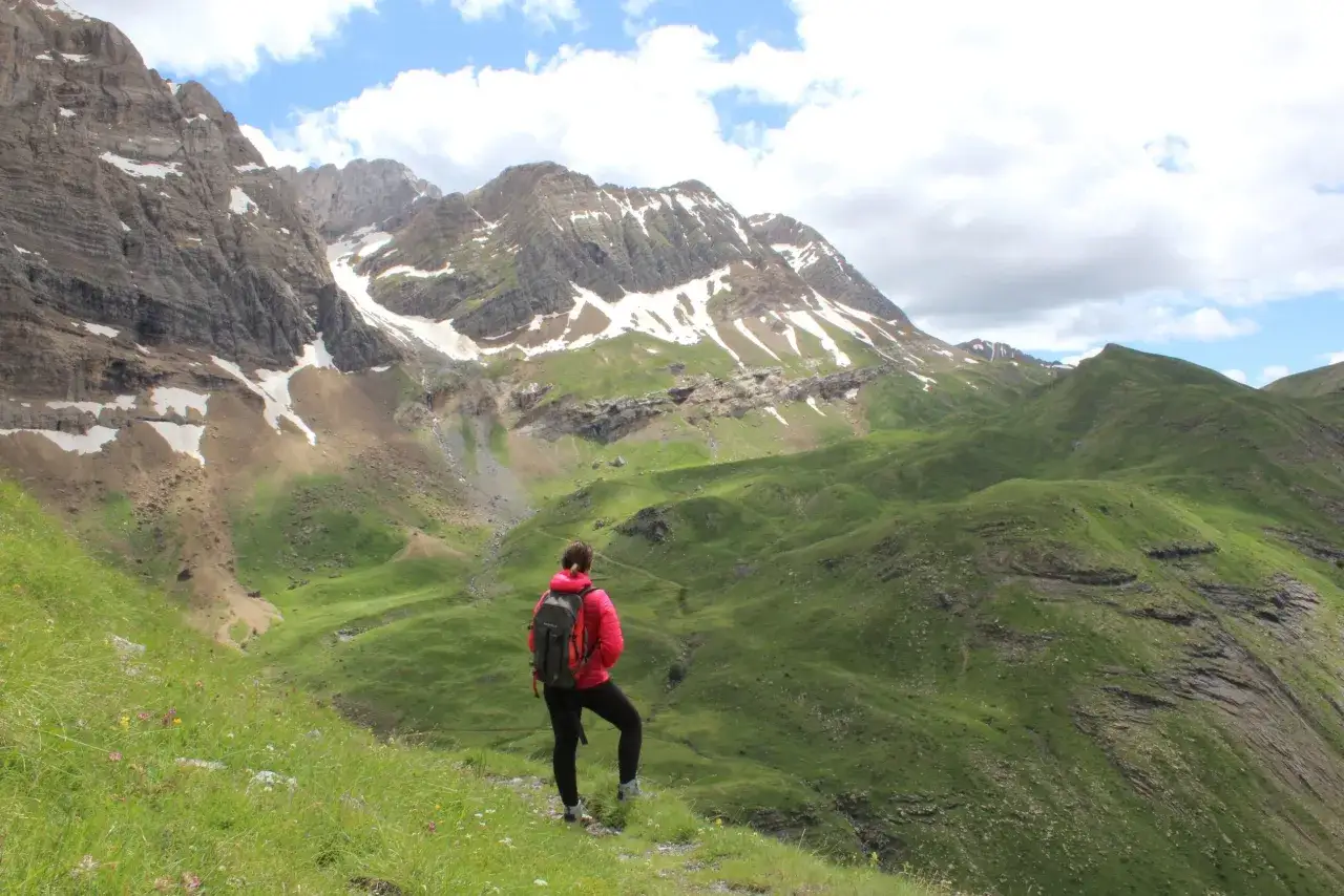Senderismo por las rutas de Panticosa, con una persona de espaldas contemplando las majestuosas monta&ntilde;as nevadas y verdes valles.